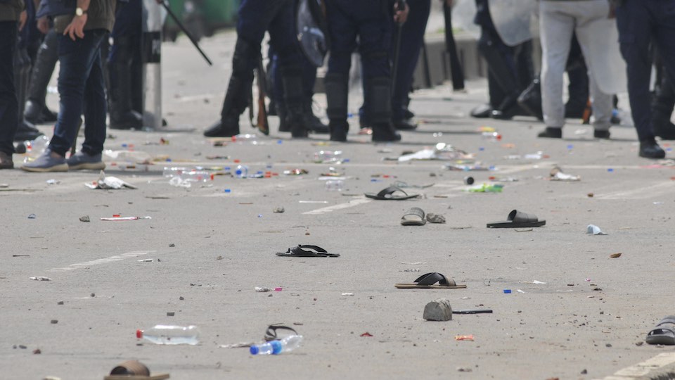 Sandalen und Flaschen von Protestierenden, dahinter Polizisten 