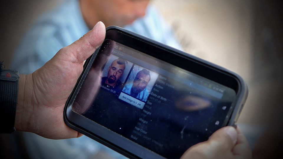 A tablet running facial recognition software in the hands of a police officer