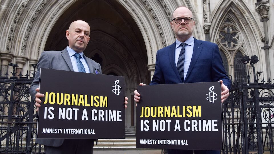 Two men hold signs that read 'Journalism Is Not a Crime'