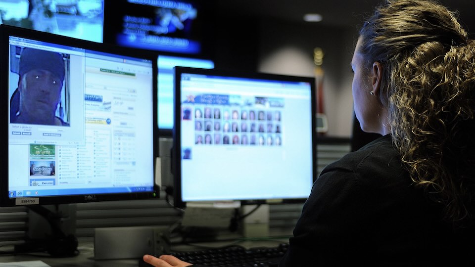 Police officer seated at a computer running a facial recognition program